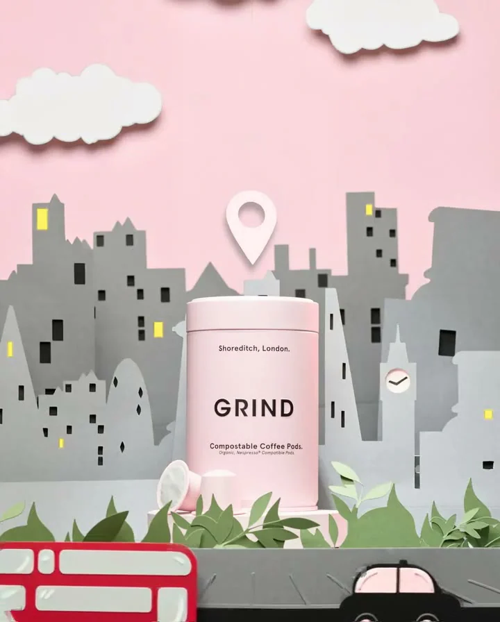 A pink GRIND tin in a handmade paper London scene with a bus and black cab.