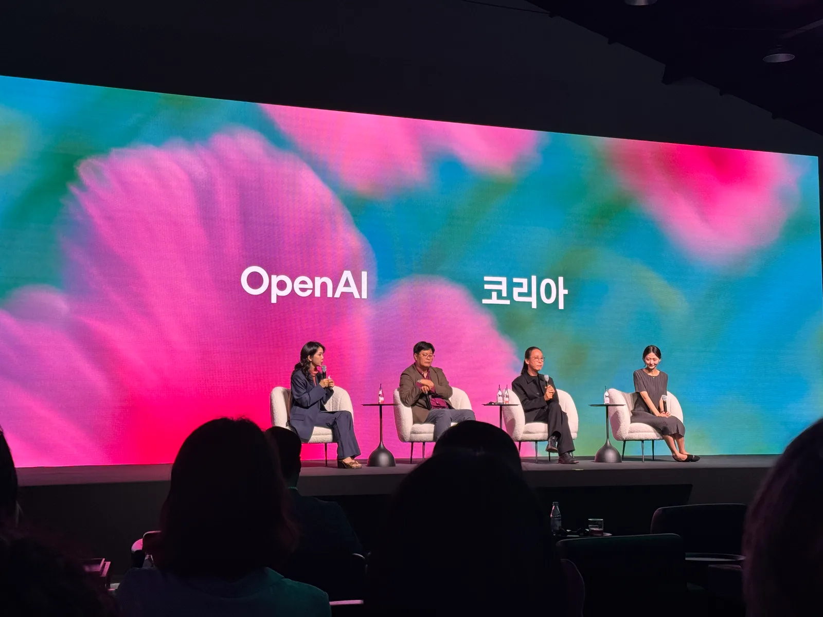 A panel of four speakers on stage in front of a large OpenAI 코리아 screen, with the audience in silhouette.